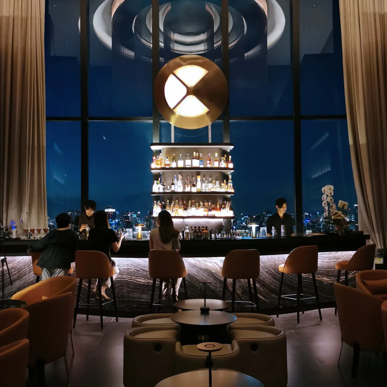 Cielo Sky Bar - indoor bar with backlit spirits shelf and floor to ceiling city view windows at night