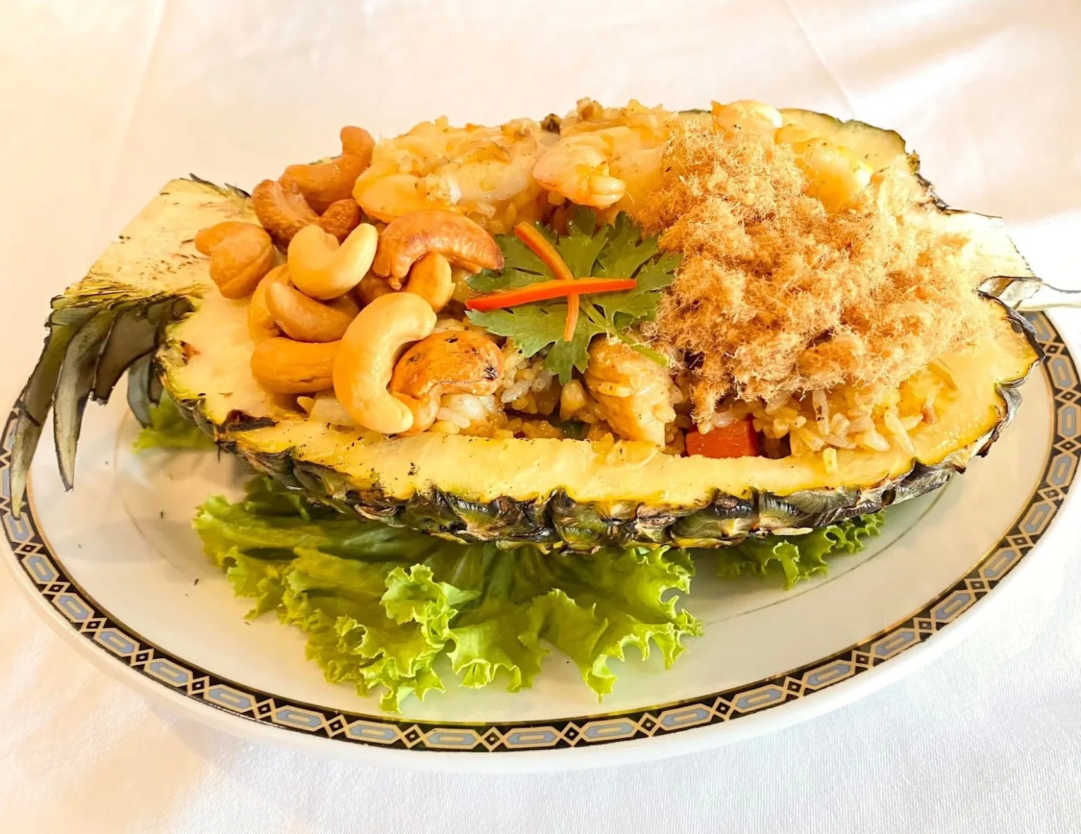 Methavalai Sorndaeng - fix pineapple fried rice with shrimp cashews and pork floss served in a carved pineapple half on lettuce plated on the restaurant s signature gold and blue rimmed china iconic thai hero dish