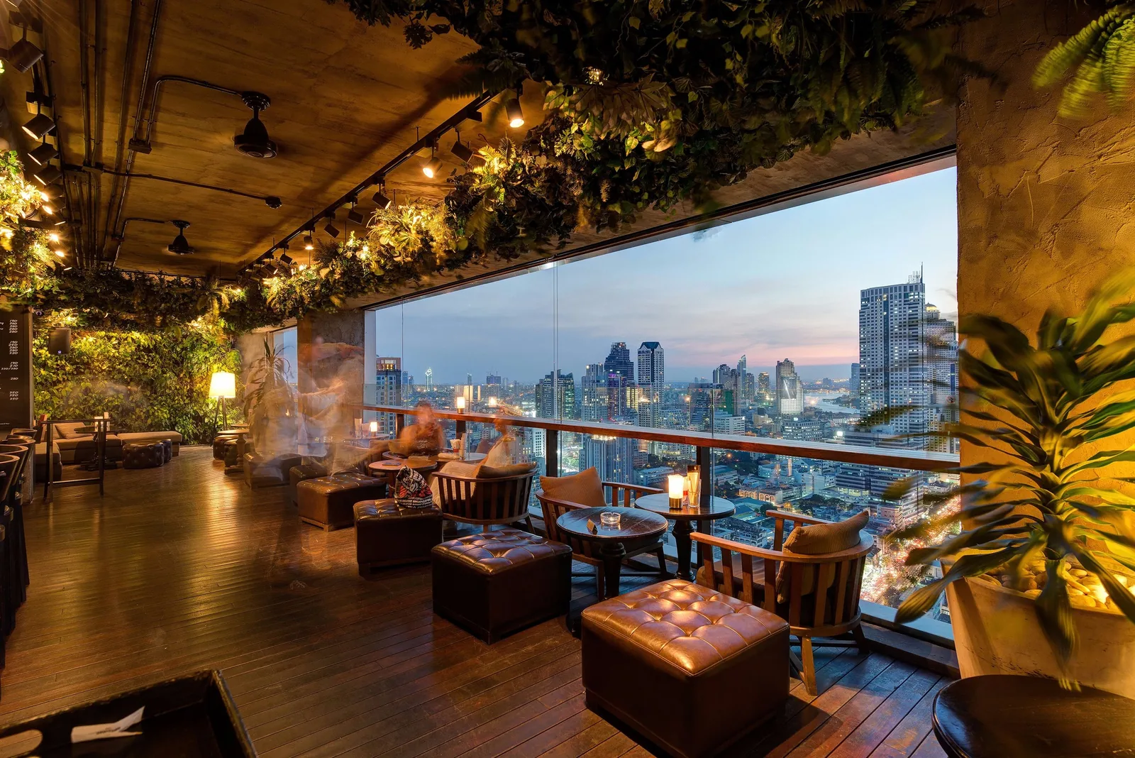 Scarlett Wine Bar - fix scarlett covered rooftop terrace lounge at dusk leather ottomans and low tables hanging greenery warm lighting panoramic floor to ceiling skyline windows