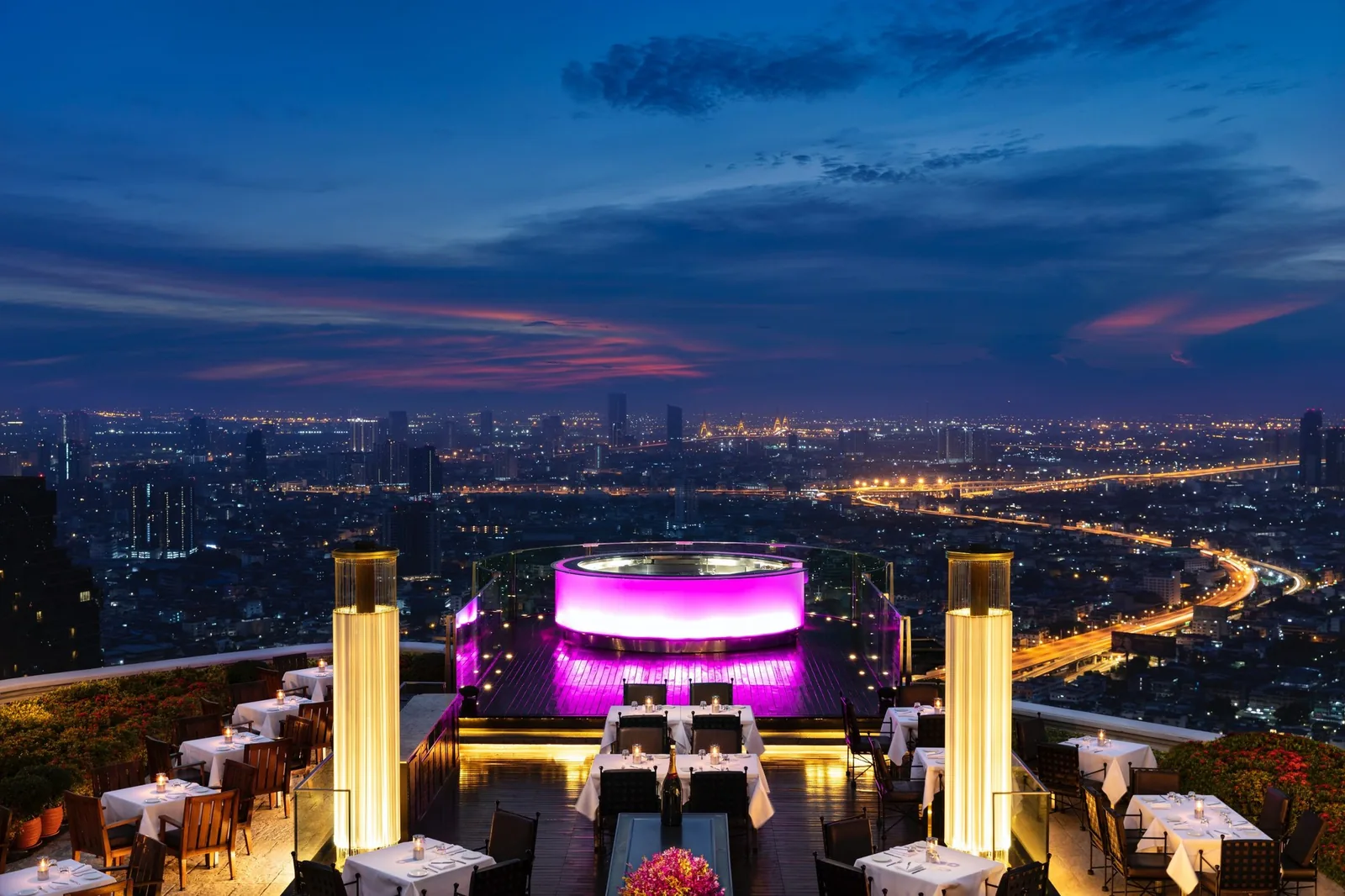 Sky Bar - fix sirocco terrace at dusk dining tables glowing gold columns signature pink lit round bar dramatic sunset skyline