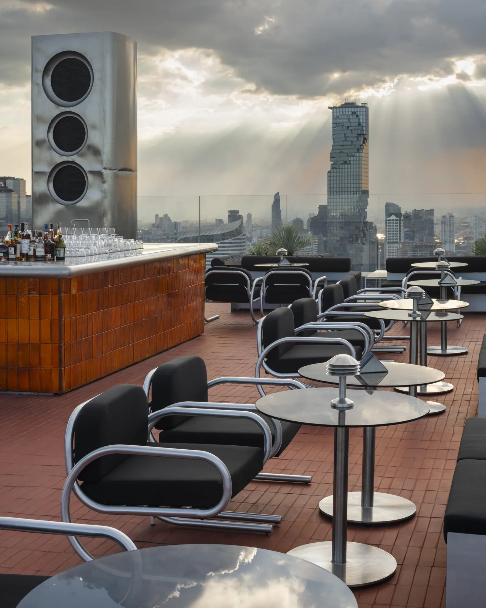 ÆTHER - fix aether rooftop deck lounge at dusk seating the brushed metal ring speaker towers and mahanakhon skyline with sunbeams
